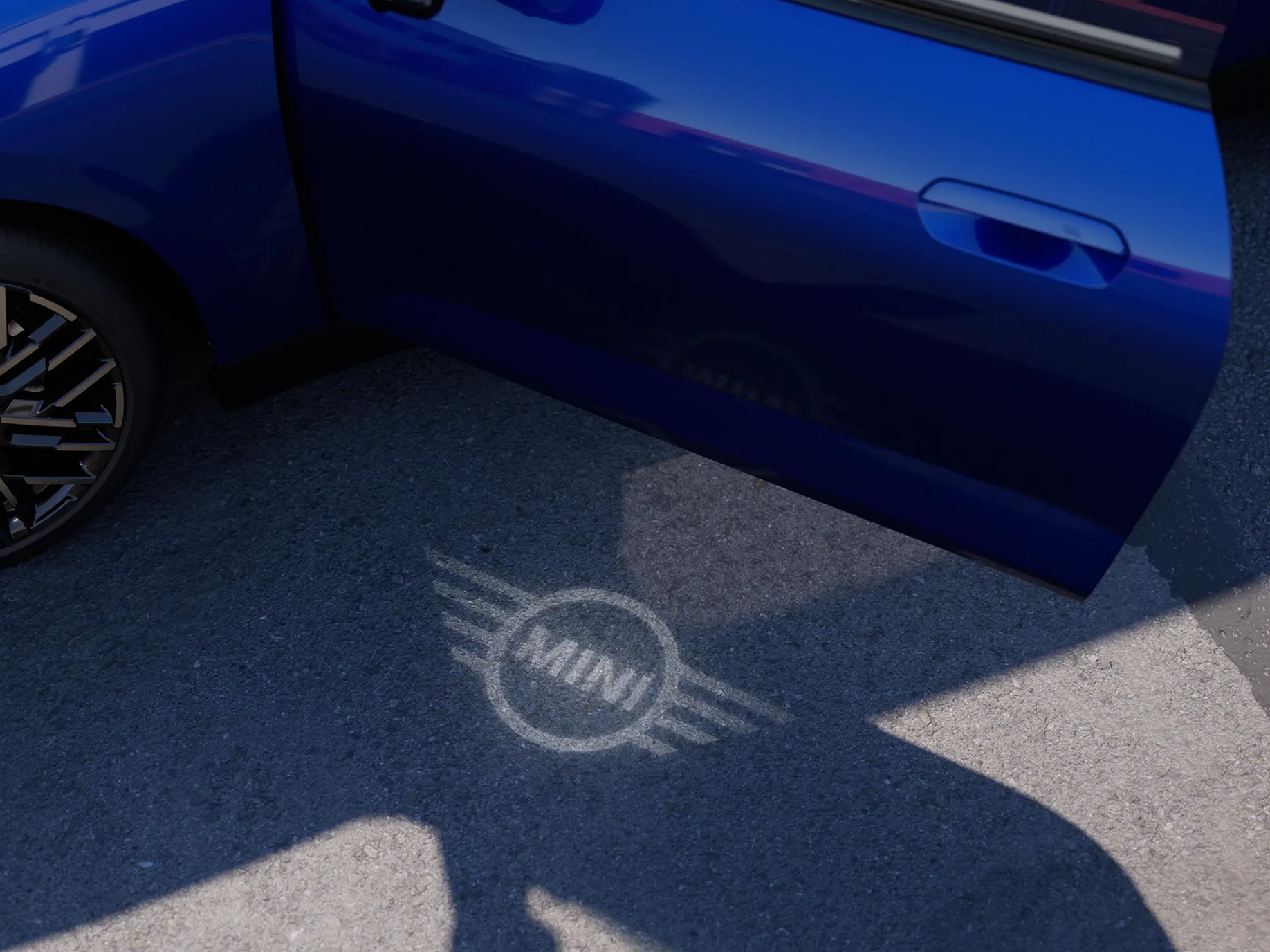 Exterior view of all-electric MINI Cooper with open door and MINI logo welcome light on the ground